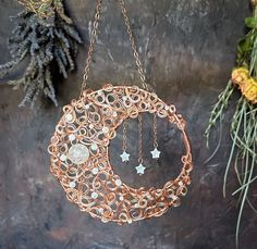 a circular metal decoration hanging from a chain next to pine cones and evergreens on a stone surface