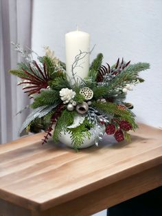 a white candle is sitting on top of a table with greenery and other decorations