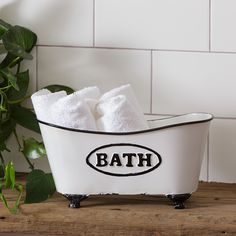 a white bath tub sitting on top of a wooden table next to a plant and toilet paper