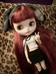 a doll with long red hair laying on top of a leopard print couch cushion, wearing a white shirt and black skirt