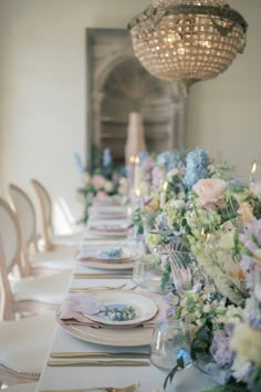 the table is set with white and blue plates, silverware, and floral centerpieces