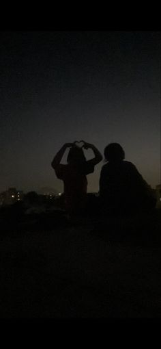 two people sitting in the dark with their backs to each other looking at the sky