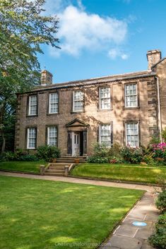 a large brick house sitting in the middle of a lush green field with trees and flowers