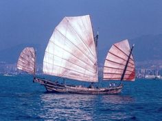 three sailboats in the ocean with mountains in the background