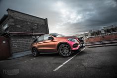 an orange and pink mercedes suv parked in a parking lot next to a brick building