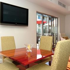 a dining room table with yellow chairs and a flat screen tv mounted on the wall