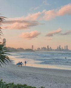 three people walking on the beach with surfboards in their hands and buildings in the background