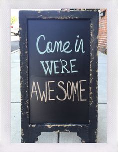 a chalkboard sign that says come in we're awesome on the side walk