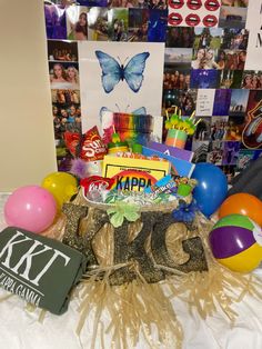 a birthday cake surrounded by balloons and other items on a table with pictures in the background