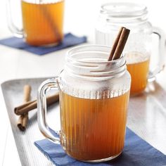 two mugs filled with hot drinks sitting on top of a blue place mat next to cinnamon sticks