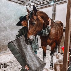 a man is standing next to a horse in a stable with a blanket on it's back