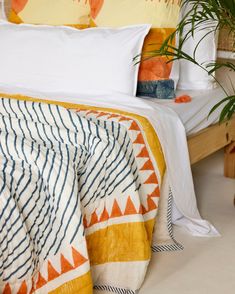 an orange and white blanket on a bed next to a potted plant