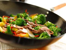 a wok filled with broccoli and meat on top of a wooden table