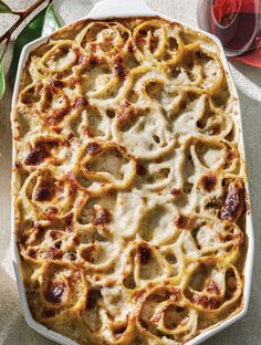 a casserole dish filled with pasta and meats next to a glass of red wine