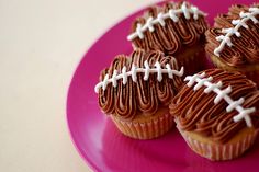 chocolate cupcakes decorated with white frosting and football decorations on a pink plate