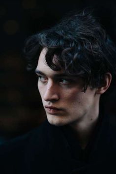 a young man with curly hair and blue eyes looks into the distance while wearing a black shirt