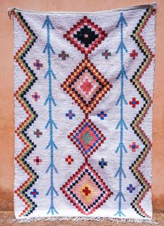 a white rug with colorful designs hanging on a wall next to a brown brick wall