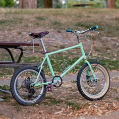 a green bike parked next to a wooden bench in front of a park with fallen leaves on the ground