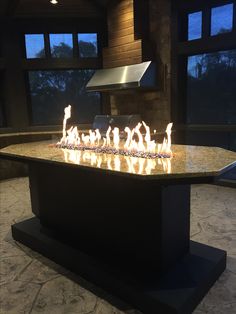 an outdoor fire pit with lots of flames on it's side and windows in the background