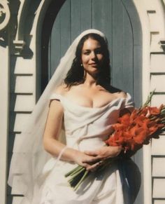 a woman in a white wedding dress holding a bouquet of flowers and wearing a veil