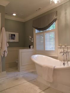 a white bath tub sitting in a bathroom next to a window with blinds on it