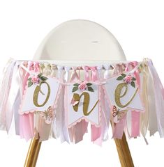 a pink and gold one first birthday banner on top of a wooden tripod stand