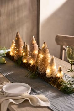 the table is set with white plates, silverware and small trees on it's edge