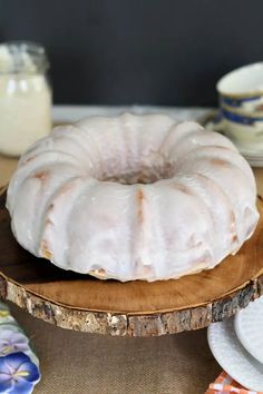 a bundt cake sitting on top of a wooden plate next to plates and cups