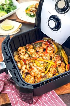 an air fryer with shrimp and peppers in it sitting on a table next to other food