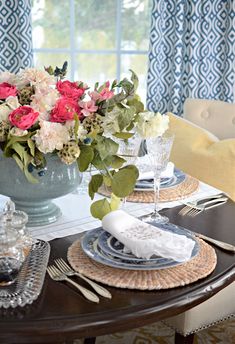 a dining room table set with place settings and flowers in a vase on the centerpiece