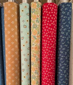 several different colored fabrics are lined up on a rack in a store, each with flowers and polka dots