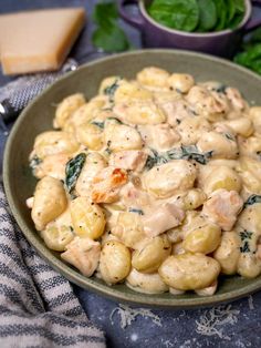 a bowl filled with pasta and spinach on top of a table next to cheese