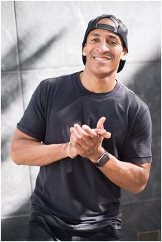 a man in black shirt and hat sitting down with his hands folded out to the side