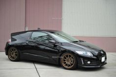 a black sports car parked in front of a pink building with gold rims on it