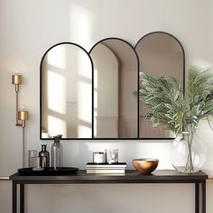 a table with three mirrors on it and a vase filled with plants next to it