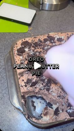 an oreo peanut butter pie in a tin on a counter with a hand reaching for it