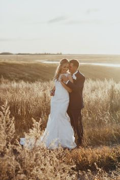 a bride and groom standing in tall grass