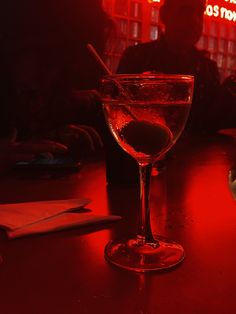 a glass filled with liquid sitting on top of a wooden table next to a red light