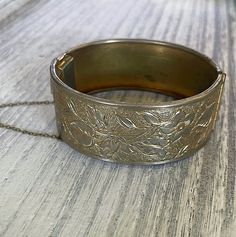 Add a touch of vintage elegance to your outfit with this beautiful Vintage Brass Hinged Bangle. The bracelet features a classic nouveau-style design with delicate floral etching, all in a stunning gold color. Approximately 1 inch tall About 2.5 inches wide Comes with original safety chain This hinged bangle is meticulously crafted and perfect for wearing alone as a statement piece or pairing with your favorite accessories. Don't miss out on adding this charming vintage piece to your collection! Elegant Antique Gold Metal Bracelets, Elegant Antique Gold Metal Bracelet, Elegant Antique Gold Bangle Bracelet, Antique Gold Adjustable Bracelets For Formal Occasions, Antique Gold Vintage Bracelet For Formal Occasions, Vintage Antique Gold Bracelets For Formal Occasions, Vintage Adjustable Bracelets With Intricate Design, Elegant Antique Gold Bangle, Antique Gold Vintage Bangle