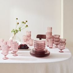 a table topped with lots of pink glass cups and saucers next to a vase filled with flowers