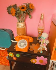 an orange phone sitting on top of a wooden table next to a vase with flowers