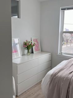 a bedroom with white furniture and pink flowers in the vase on the dresser next to the bed