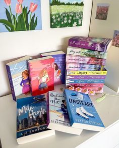 a stack of books sitting on top of a white desk next to pictures and paintings