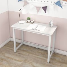 a white desk with an open book on it in front of a pink and white wall