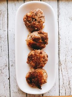 three meat patties on a white plate with a wooden table in the back ground