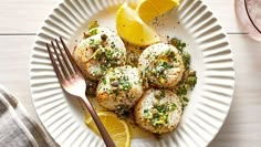 a white plate topped with scallops and lemon wedges next to a fork