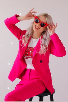 a woman sitting on top of a stool wearing pink pants and a bright pink blazer