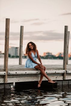 a woman is sitting on a dock by the water