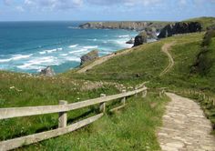 a wooden path leading to the ocean on top of a grassy hill next to water