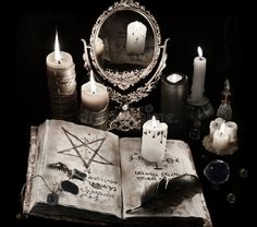 an open book sitting on top of a table next to candles and other items in front of a mirror